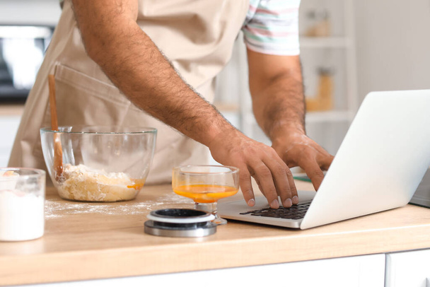 Όμορφος άνθρωπος χρησιμοποιώντας φορητό υπολογιστή, ενώ το μαγείρεμα στην κουζίνα, closeup - Φωτογραφία, εικόνα