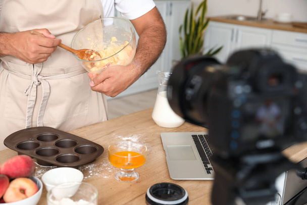 Handsome man preparing peach muffins and recording video tutorial in kitchen - Foto, Imagen
