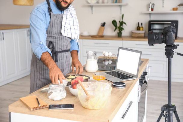 Красивий чоловік готує персикові кекси і записує відео-підручник на кухні
 - Фото, зображення