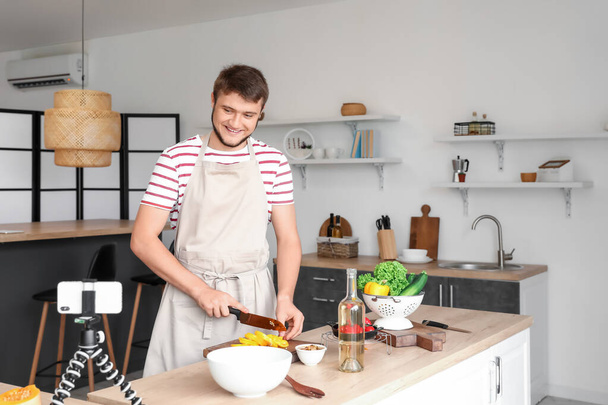 Jeune homme coupe poivron tout en enregistrant tutoriel vidéo de cuisine - Photo, image