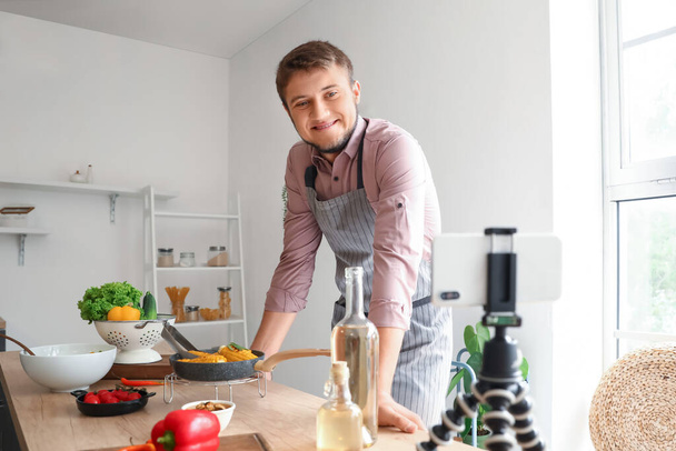 Mladý muž nahrávání vaření video tutorial na mobilním telefonu v kuchyni - Fotografie, Obrázek