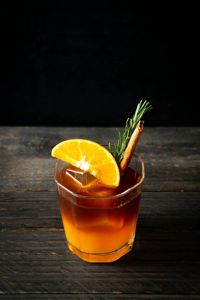 A glass of iced americano black coffee and layer of orange and lemon juice decorated with rosemary and cinnamon - Fotó, kép
