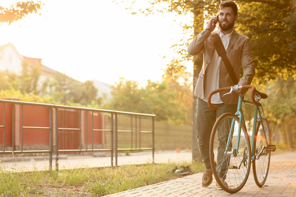 Молодий бородатий бізнесмен з велосипедом розмовляє мобільним телефоном на міській вулиці
 - Фото, зображення