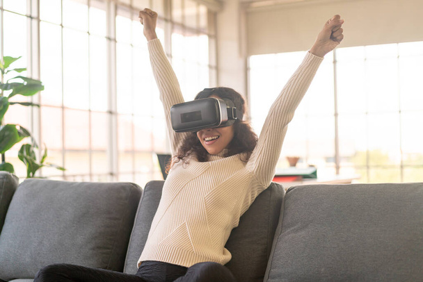 Latin woman using a virtual reality headset on sofa at home - Valokuva, kuva