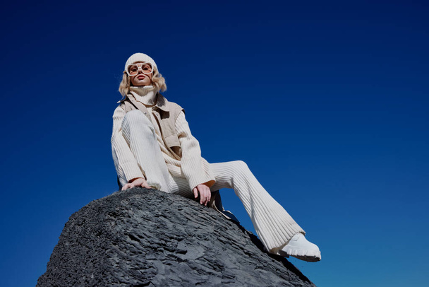 νεαρή γυναίκα κάθεται σε ένα πέτρινο γαλάζιο ουρανό σε ένα καπέλο χαλάρωση - Φωτογραφία, εικόνα