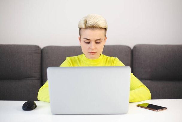 Entrepreneur businesswoman working on computer at home. Focused young female typing text on laptop keyboard. Tom boy person with dyed short hair doing distant work online with fast internet - 写真・画像