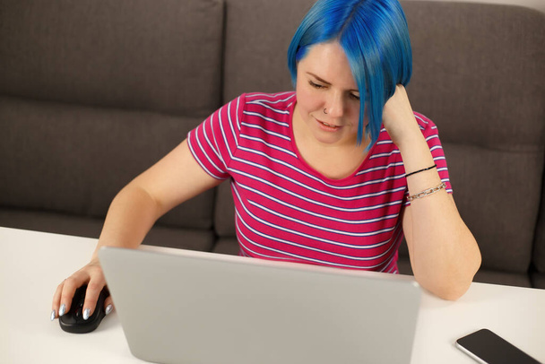 Young white woman with blue hair working on laptop computer. Cute Caucasian female with colored bob hairstyle using modern notebook pc for online work and communication during lockdown - Foto, afbeelding