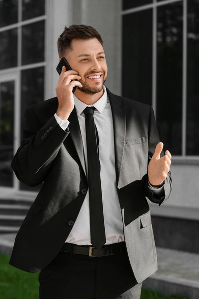 Stylowy biznesmen rozmawiający przez telefon komórkowy w pobliżu biurowca - Zdjęcie, obraz