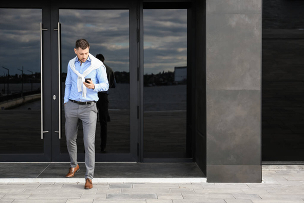 Schöner Geschäftsmann benutzt Handy in der Nähe von Bürogebäude - Foto, Bild