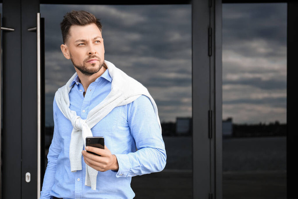 Hombre de negocios guapo con teléfono móvil cerca del edificio de oficinas - Foto, imagen