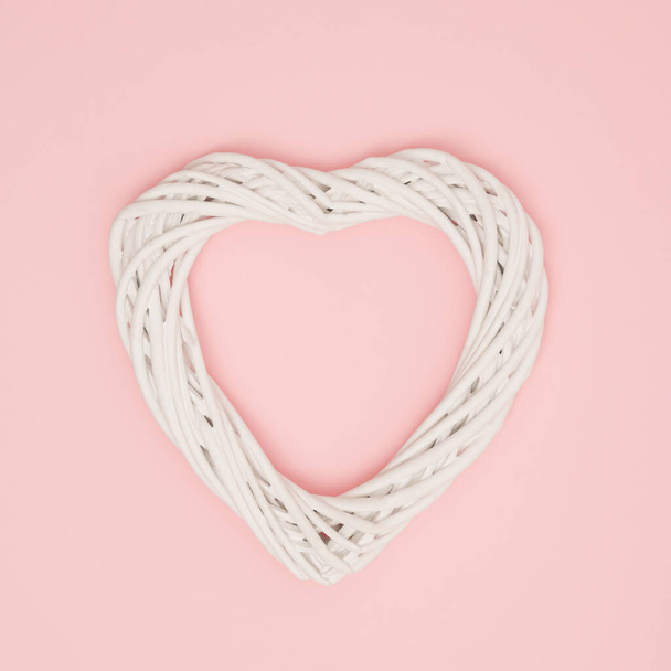 A heart made of knitted white wicker on a pastel pink background. Minimal creative concept of decorative infatuation, love, Valentine's Day, weddings. - Fotografie, Obrázek