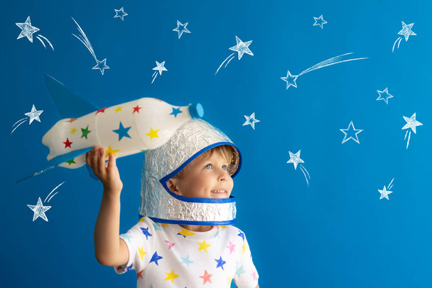 Happy child playing with toy rocket against blue background. Kid pretend to be astronaut. Imagination and children dream concept - Фото, изображение