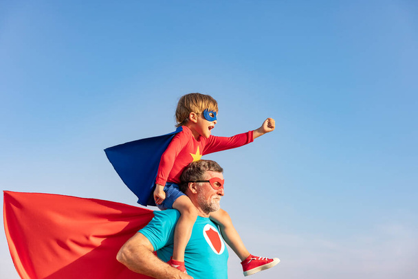 Superhero senior man and child playing outdoor. Super hero grandfather and boy having fun together against blue summer sky background. Family holiday concept. Happy Father's day - Φωτογραφία, εικόνα