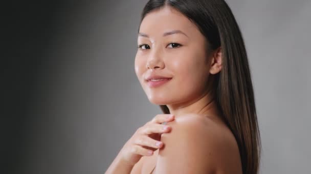 Perfekte körperliche Verfassung. Junge selbstbewusste, hemdlose asiatische Frau streichelt ihre perfekte Haut, grauer Studiohintergrund - Filmmaterial, Video