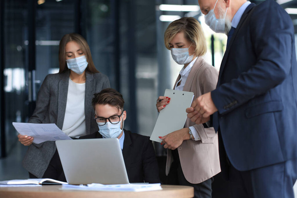 Business people wearing protective face masks while holding a presentation on a meeting during coronavirus epidemic - Фото, изображение