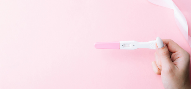 Kit de teste de gravidez. Mão feminina segurar positivo teste grávida com fita de seda em fundo rosa. Medicina ginecológica, gravidez fertilidade maternidade pessoas conceito - Foto, Imagem