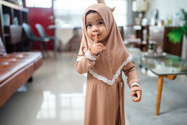 kid with hushing gesture wearing muslim headscarf at home - Foto, imagen