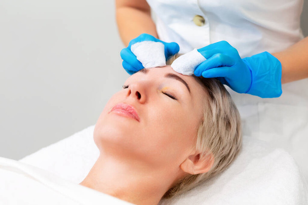 Egy profi kozmetikus mechanikai tisztítást végez az ügyfél arcán. Az eljárás, hogy megszabaduljunk a pattanásoktól. A koncepció szalon bőrápolás. - Fotó, kép