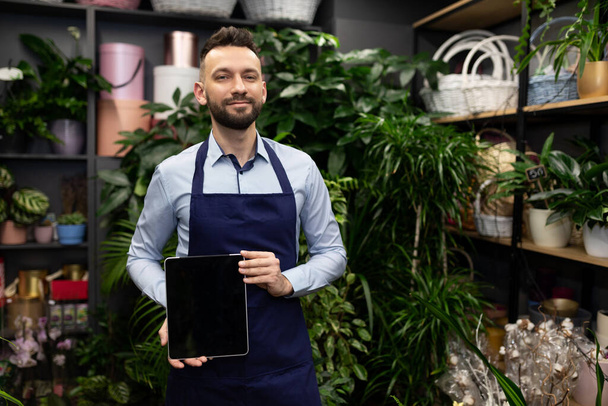nerd at flower shop demonstrating tablet screen next to shelves with potted plants - 写真・画像