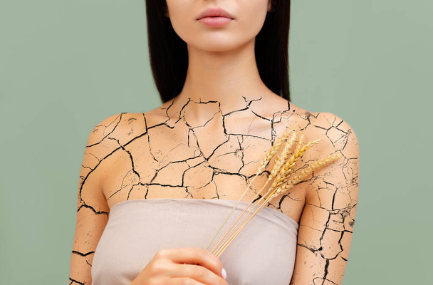 Suchá kůže na těle. Portrét ženy s pšeničným uchem v rukou a kůží pokrytou prasklinami. Koncept kožních onemocnění. - Fotografie, Obrázek