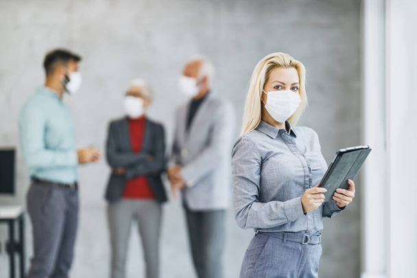 Retrato de una empresaria confiada con máscara protectora usando tableta digital en la oficina durante la pandemia del virus corona. Mirando la cámara. - Foto, Imagen