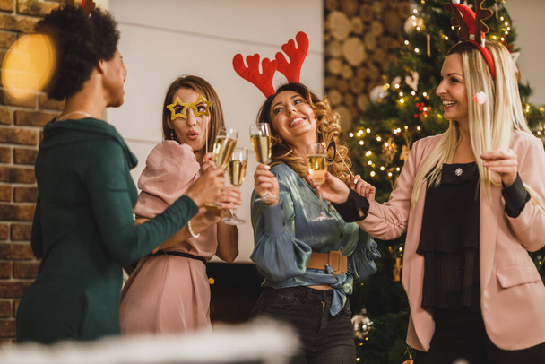 Fröhliche multietnische Mädchen haben Spaß beim gemeinsamen Anstoßen mit Champagner auf Weihnachten oder Neujahr. - Foto, Bild