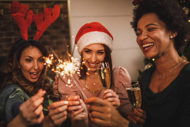 Iloiset monikäyttöiset tytöt leikkivät tähtisadetikuilla ja paahtavat samppanjalla jouluna tai uudenvuoden kotijuhlissa.. - Valokuva, kuva