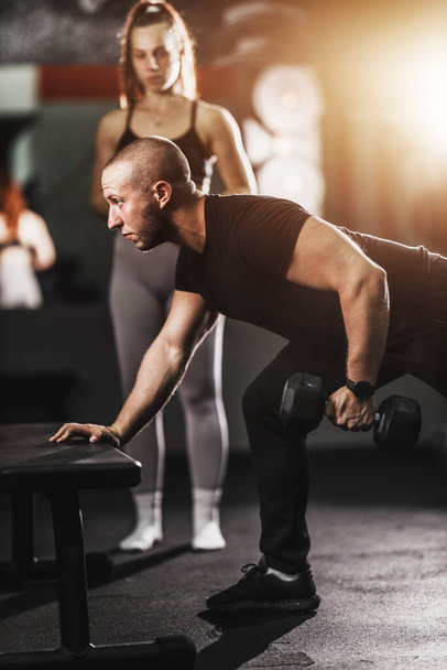 Instructor de fitness mostrando ejercicio para el músculo de la espalda a una joven en forma en el entrenamiento en un gimnasio. - Foto, Imagen
