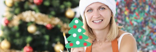 Noel Baba şapkalı kadın sanatçı elinde oyuncak Noel ağacı ve boya fırçası tutuyor. - Fotoğraf, Görsel