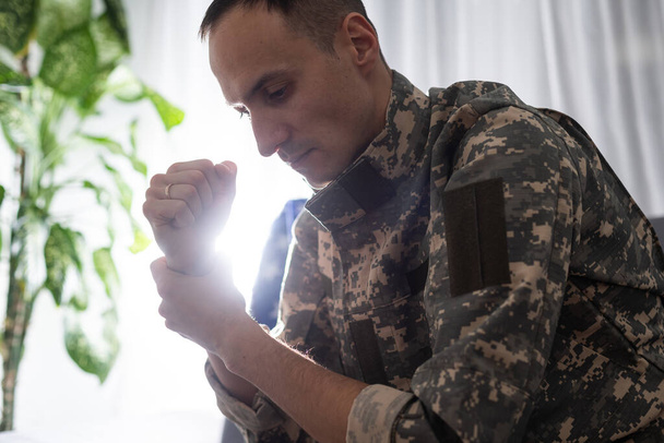 λυπημένος στρατιώτης με στολή καμουφλάζ κρατώντας στρατιωτική ετικέτα σε σφιγμένα χέρια - Φωτογραφία, εικόνα