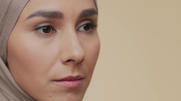 Κοντινό πλάνο πορτρέτο της νεαρής σοβαρής μουσουλμανικής γυναίκας στην παραδοσιακή μαντίλα κοιτάζοντας στην άκρη, μπεζ φόντο, κενό χώρο - Πλάνα, βίντεο