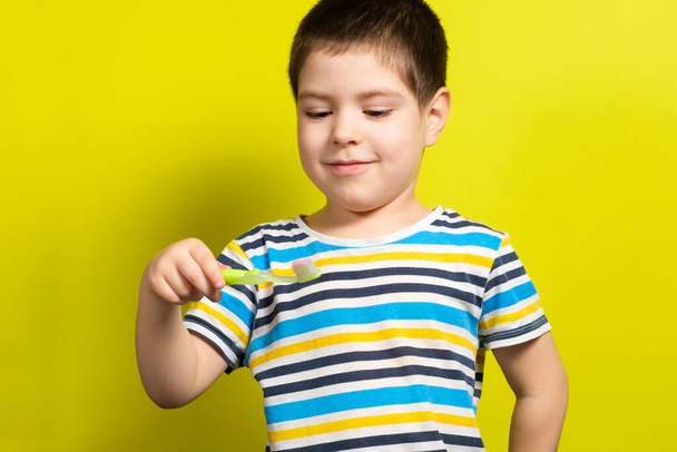 A handsome boy of 4 years old holds a toothbrush on a yellow background and laughs, copy space for text - Fotoğraf, Görsel