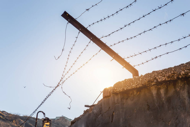 Yakın çekim cezaevi ya da sınır betonu eskimiş çit paslı dikenli tel zincir güvenlik bariyeri silueti gökyüzü güneşi arka planı. Diktatörlük zorbalık rejimi özgürlük kavramını sonlandırdı - Fotoğraf, Görsel