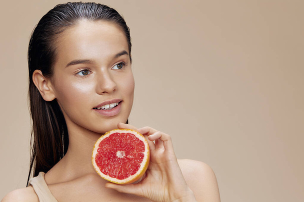 brunette grapefruit in de buurt van gezicht schoon huidverzorging gezondheid geïsoleerde achtergrond - Foto, afbeelding