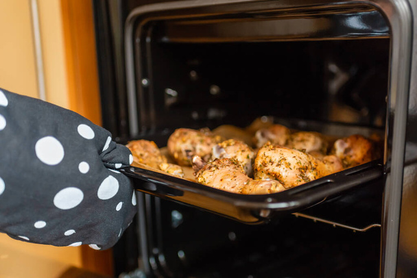 Vrouwenhand trekt gebakken kippenpoten uit de oven. Zachte focus, selectieve focus. - Foto, afbeelding