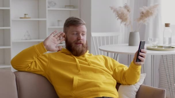 Видео с бородатым парнем, звонящее через сотовый телефон и машущее рукой в помещении - Кадры, видео
