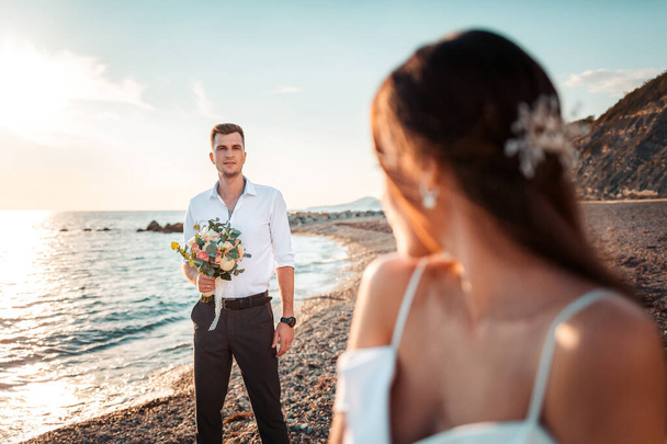 Groom holding a bouqet and admires his beautiful bride. Woman turn around and looking at him. The Wedding Day. - Valokuva, kuva
