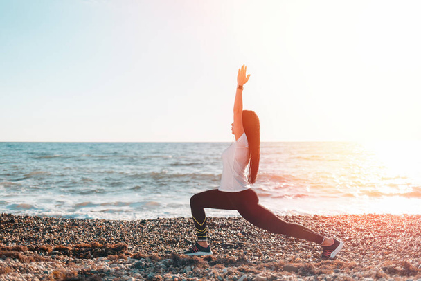 Le concept du yoga et des sports de plein air. Une jeune femme qui fait du yoga sur une plage rocheuse. Copier l'espace et la lumière. - Photo, image