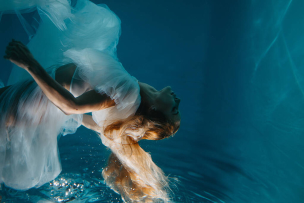 Beautiful woman in bridal dress swims and dives under sunlit deep water. Closeup. - Фото, изображение