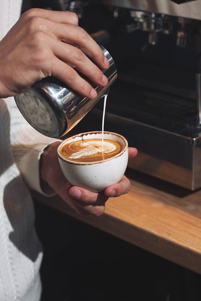 Close up hand of man barista pouring froth milk in espresso coffee in coffee cup making caffe latte art serve to customer. Small business cafe and restaurant owner and part time job working concept - 写真・画像