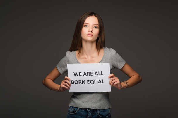young brunette woman holding placard with we are all born equal lettering isolated on grey - Photo, Image