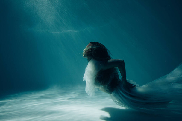 Piękna kobieta w sukni ślubnej pływa i nurkuje pod słońcem głębokiej wody. - Zdjęcie, obraz