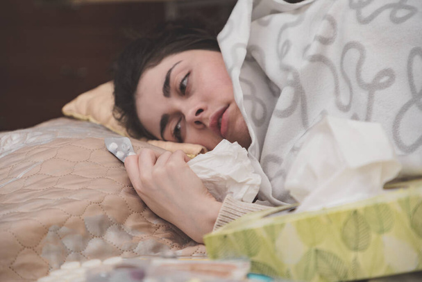 インフルエンザで病気になった少女はベッドに横になって薬を手に. - 写真・画像