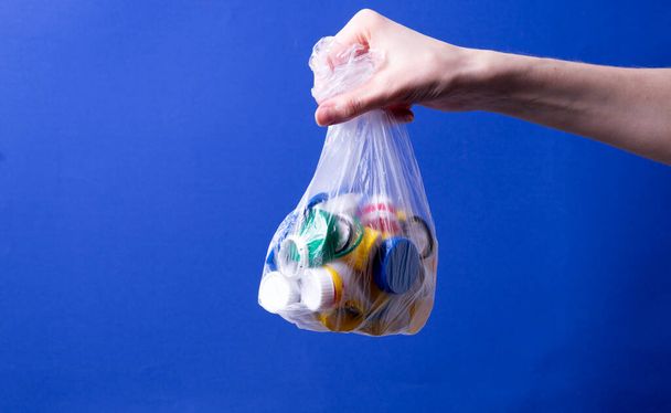 la mano de una mujer sostiene una bolsa con tapas de plástico para reciclar - Foto, imagen