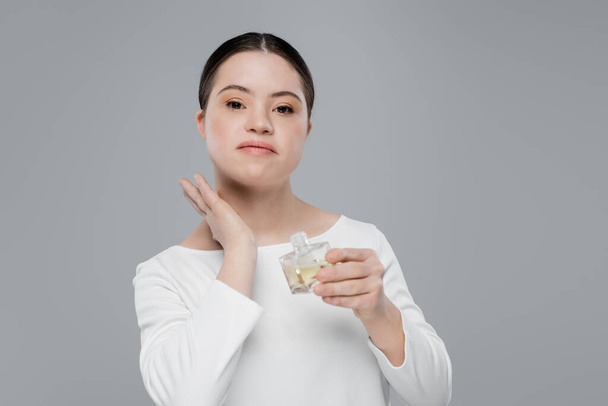 Mujer joven con síndrome de Down aplicando perfume aislado en gris  - Foto, Imagen