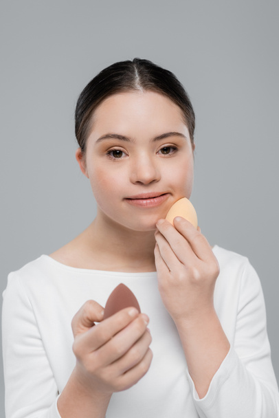 Woman with down syndrome holding beauty blenders isolated on grey  - Foto, Imagem