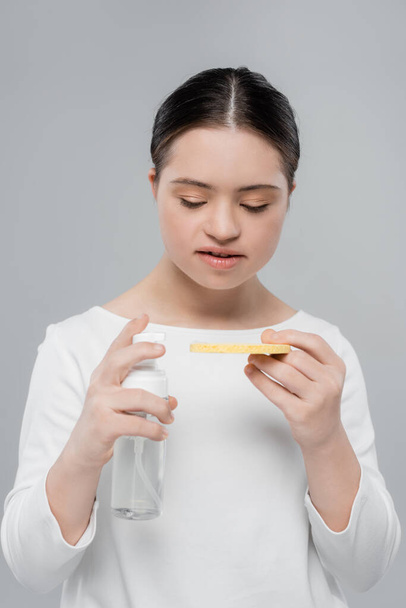 Жінка з синдромом вниз тримає губку і очищає піну ізольовано на сірому
  - Фото, зображення