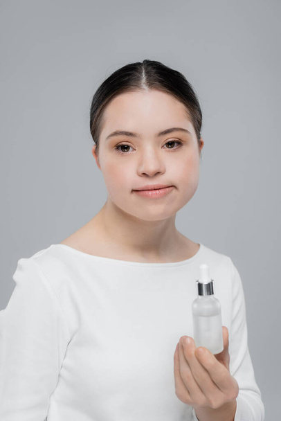 Mujer joven con síndrome de Down sosteniendo suero aislado en gris  - Foto, Imagen