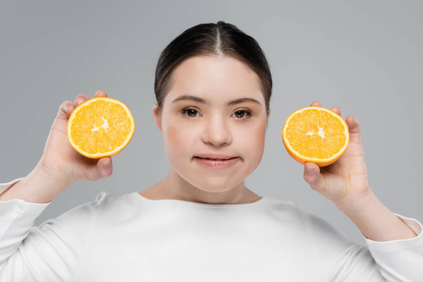 Uśmiechnięta kobieta z zespołem Downa trzymająca pomarańczę odizolowaną na szaro  - Zdjęcie, obraz