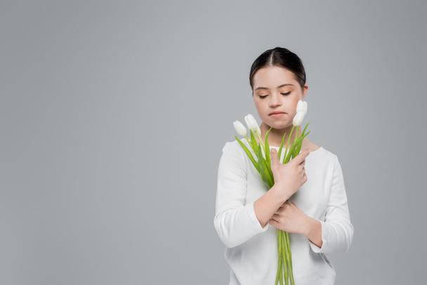 Woman with down syndrome holding flowers isolated on grey  - Foto, afbeelding